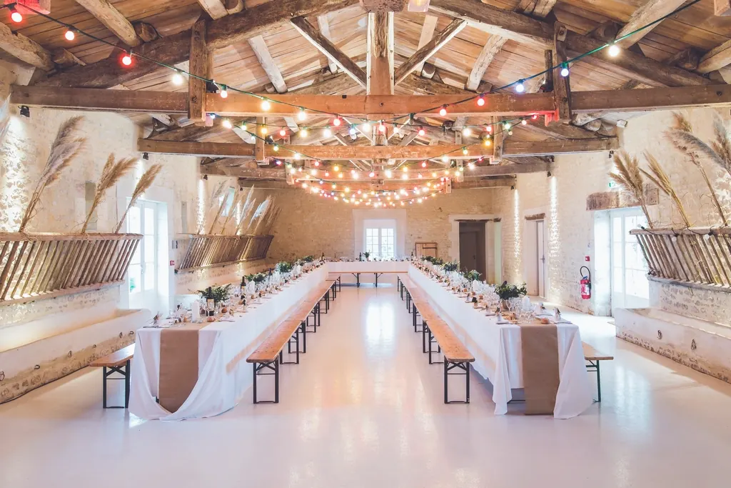Long reception tables and benches beneath festoon lights in a timber-beamed hall