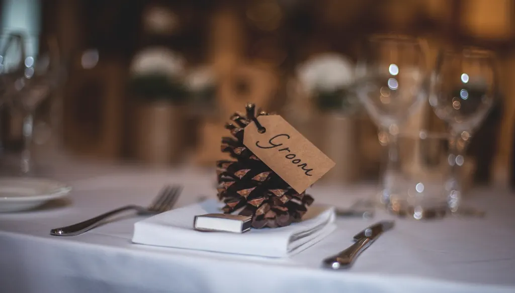 A handwritten place card on a pine cone beside cutlery and glassware