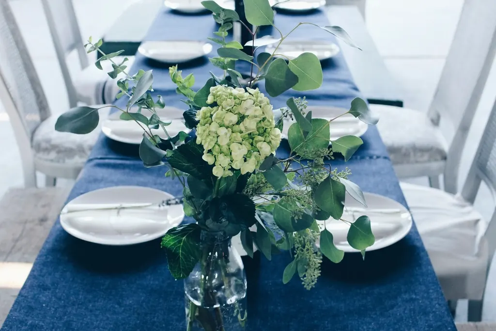A styled table with a blue runner, white plates and loose greenery