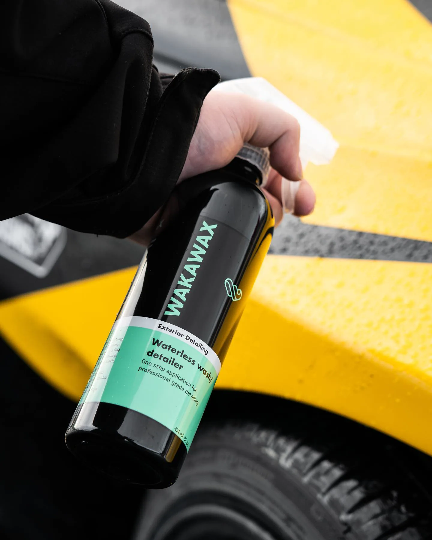 A hand holding the WakaWax bottle beside a yellow car
