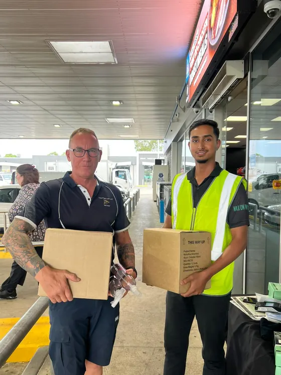 A customer and a WakaWax seller each holding a box of WakaWax at a service station