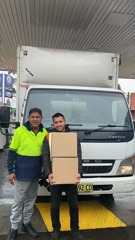 A truck driver and a WakaWax seller holding boxes in front of a white truck
