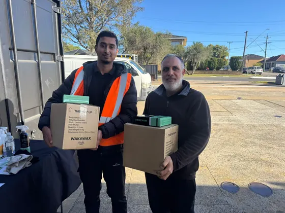 Two men holding boxes of WakaWax in a car park